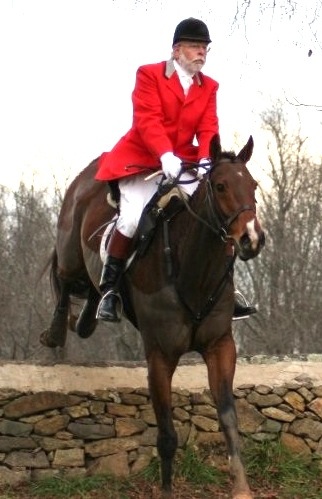 J. Harris Anderson in foxhunting attire on his horse jumping a stone wall